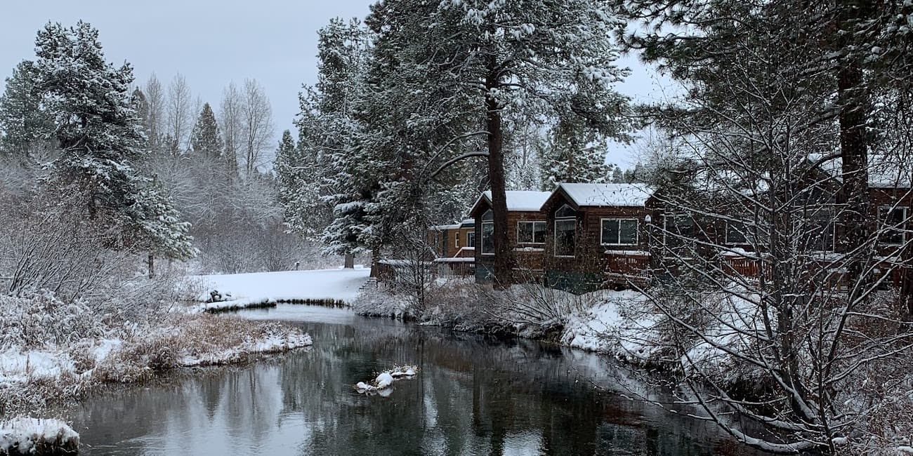 Row of snow-covered cabins across Fort Creek in winter at Crater Lake Resort