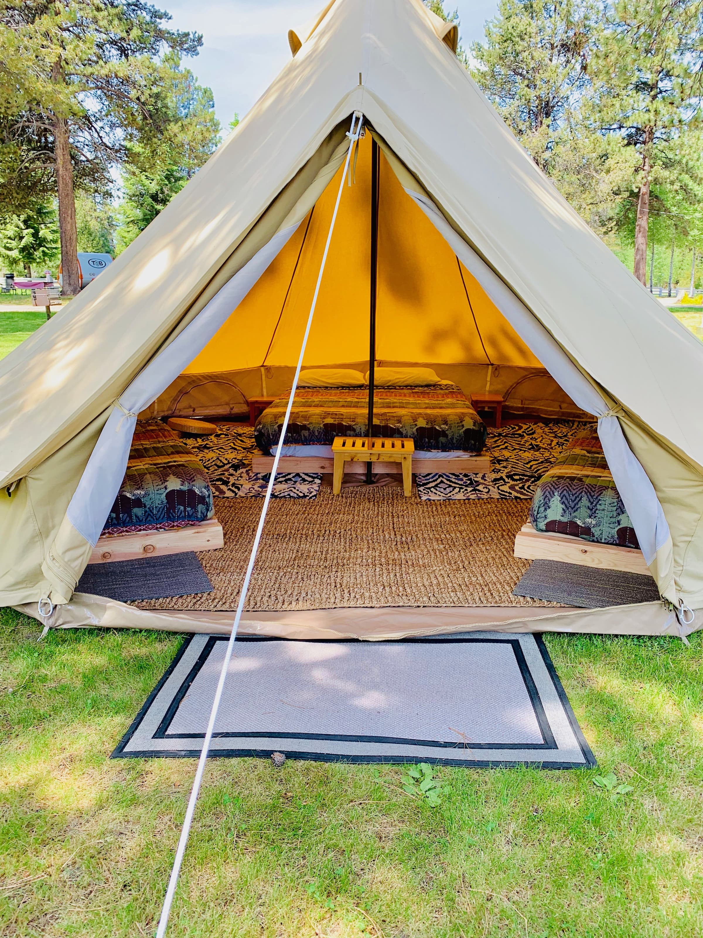 Canvas bell tent with the flap open — queen bed, two twins, jute rugs, lantern inside