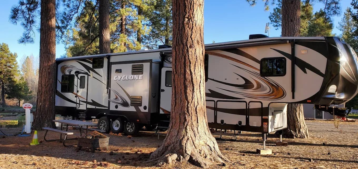 Fifth-wheel RV parked between tall pines at Crater Lake Resort