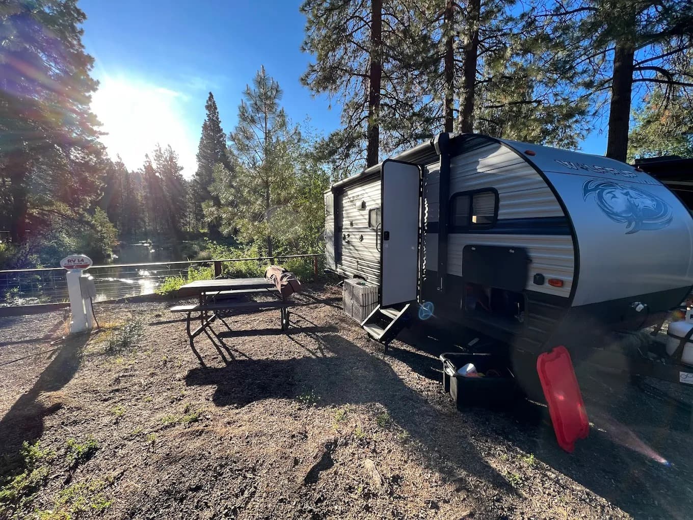 Travel trailer at a creekside RV site with sun flare through the pines