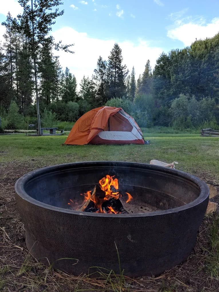 Fire ring burning at golden hour with orange tent and Fort Creek in the background